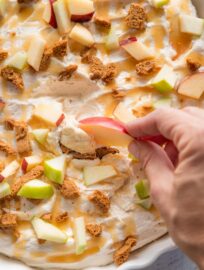 Apple slice scooping up a bite of caramel apple cheesecake dip.