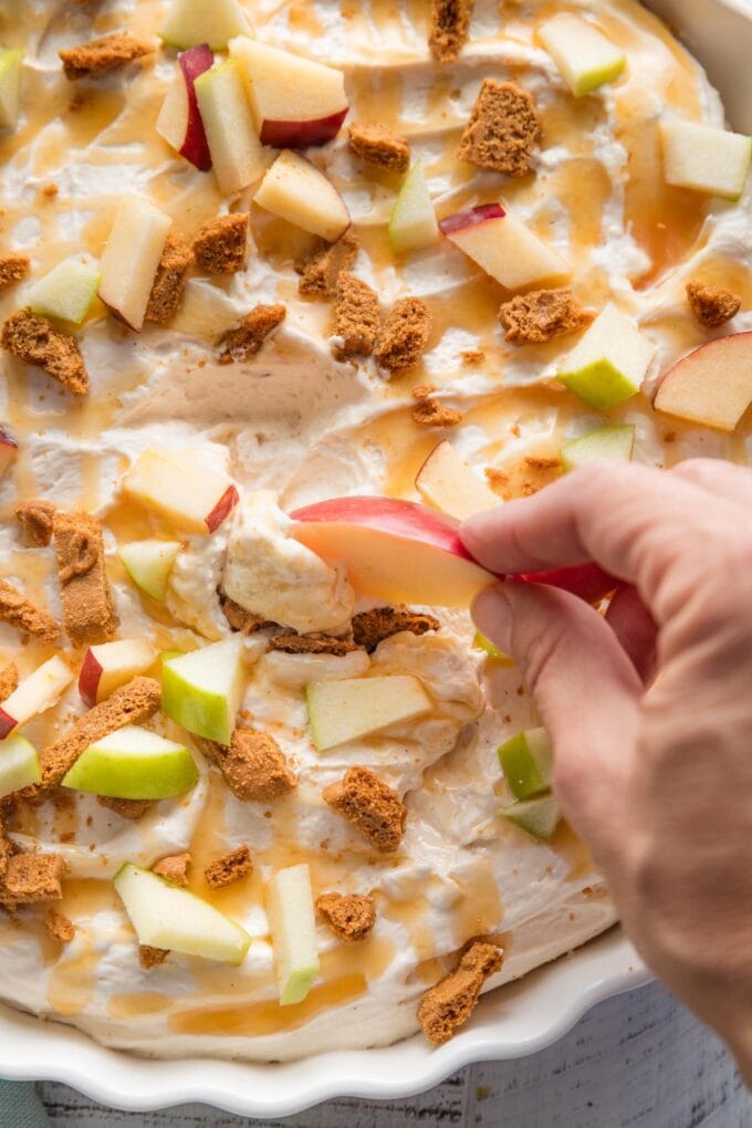 Apple slice scooping up a bite of caramel apple cheesecake dip.