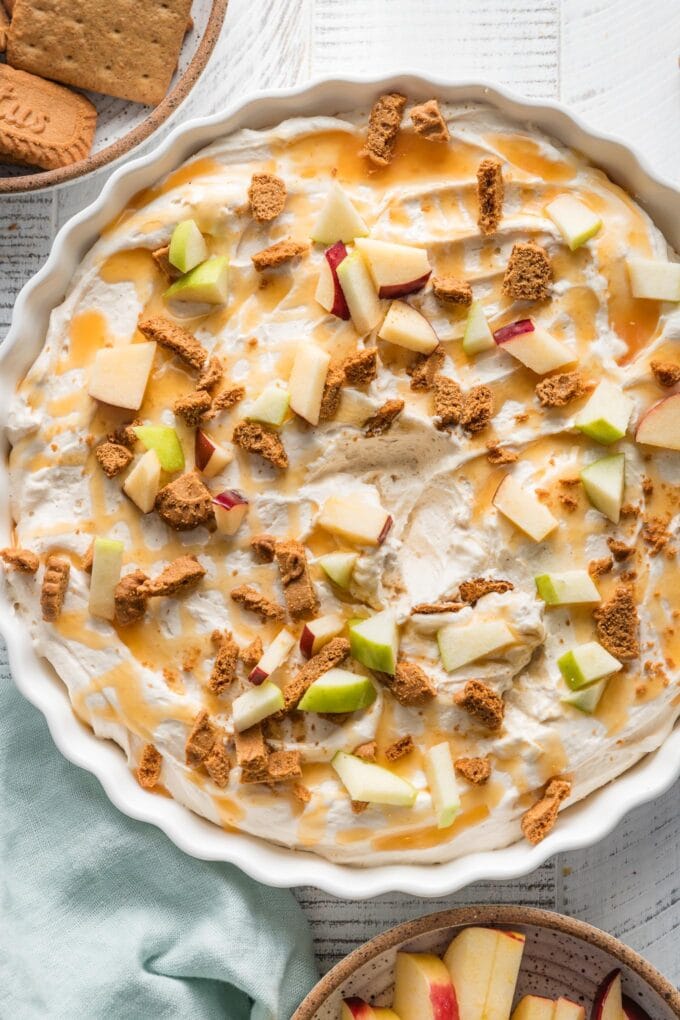 Large fluted tart pan filled with a caramel apple cheesecake dip topped with extra caramel sauce, sea salt, apple chunks, and crumbled Biscoff cookies.