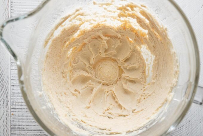 Cream cheese, brown sugar, vanilla, and a pinch of salt mixed together in a clear glass bowl.