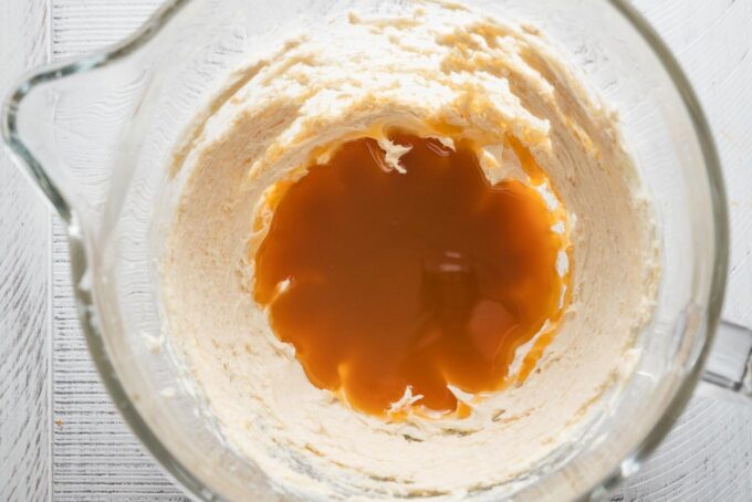 Caramel sauce added to a cream cheese mixture in a clear glass bowl.