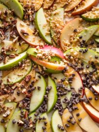 Close up of caramel apple slices topped with toffee bits, pecans, and chocolate chips.