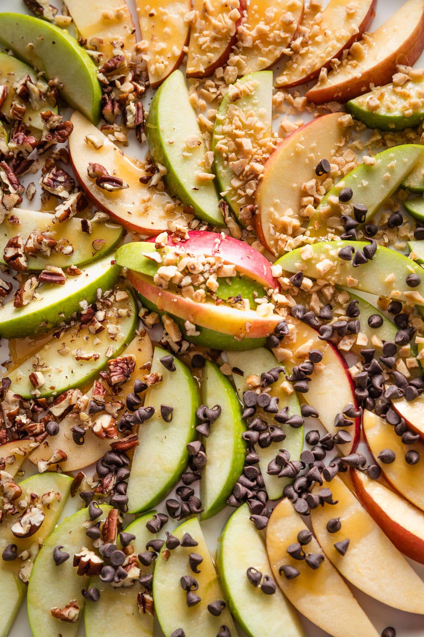 Close up of caramel apple slices topped with toffee bits, pecans, and chocolate chips.