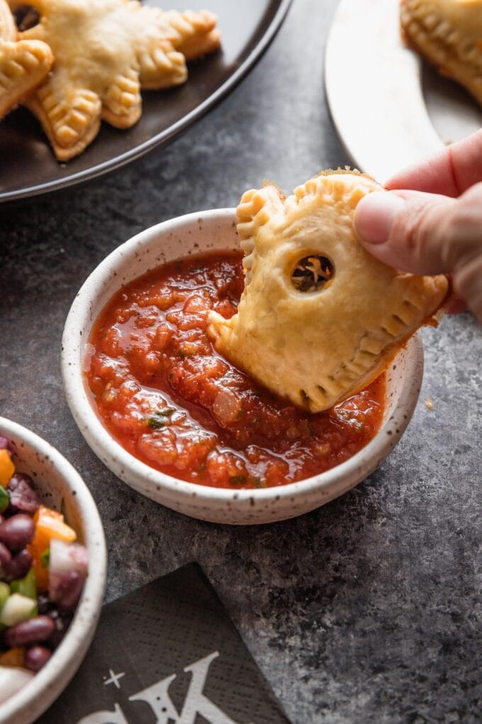 A small ghost-shaped taco hand pie being dipped into salsa for a Halloween-themed savory snack.