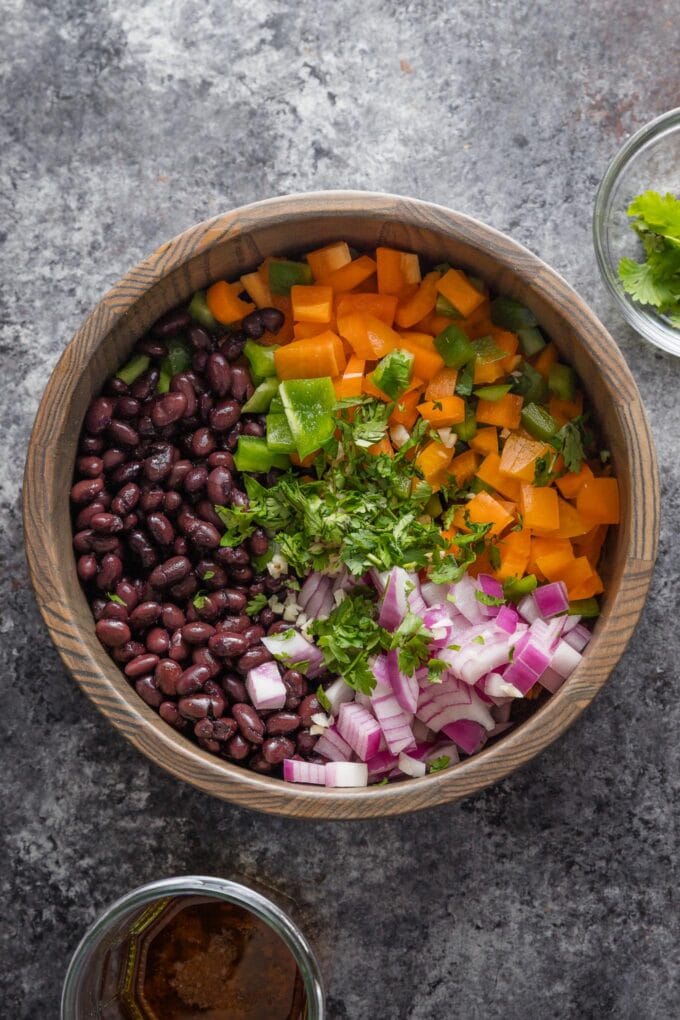 Black beans, diced bell pepper, red onion, and cilantro combined in a dark wooden bowl.