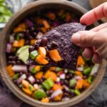Halloween-inspired black bean dip served with blue corn tortilla chips in a dark wooden bowl.