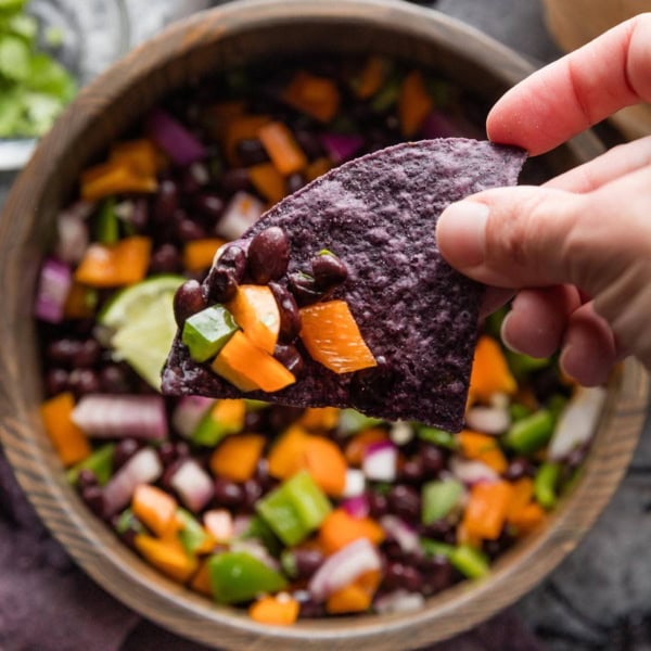 Halloween-inspired black bean dip served with blue corn tortilla chips in a dark wooden bowl.