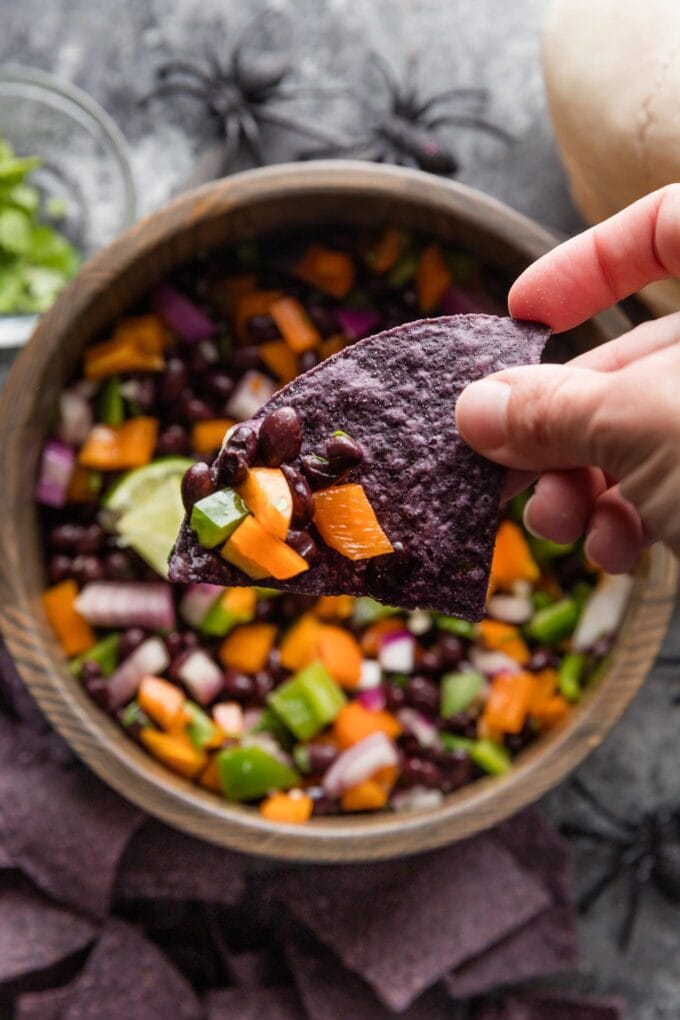 Halloween-inspired black bean dip served with blue corn tortilla chips in a dark wooden bowl.