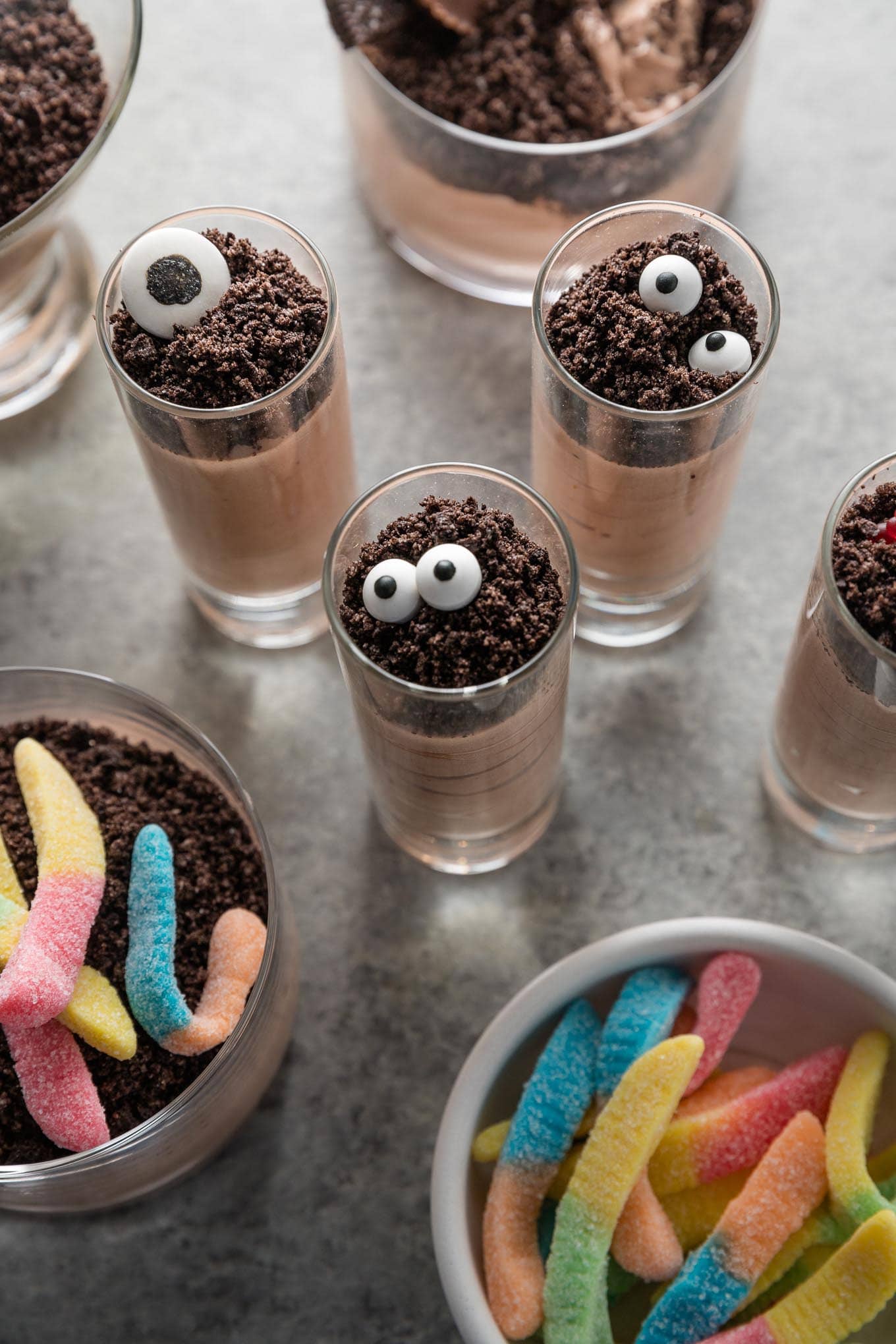 Small, tall shooter-style glasses filled with chocolate pudding and topped with crushed Oreos and candy eyeballs to make Halloween-inspired dirt cup shooters.