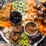 Overhead view of a large cheese board with a Halloween theme including one-eyed kiwi slices, cantaloupe bats, monster cucumber slices, and more.
