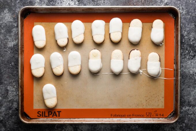 Milano cookies partially dipped in white chocolate and set on a silicone-lined baking sheet to dry.