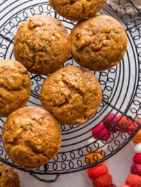 Large pumpkin zucchini muffins cooling on a black wire rack.