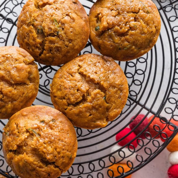 Large pumpkin zucchini muffins cooling on a black wire rack.