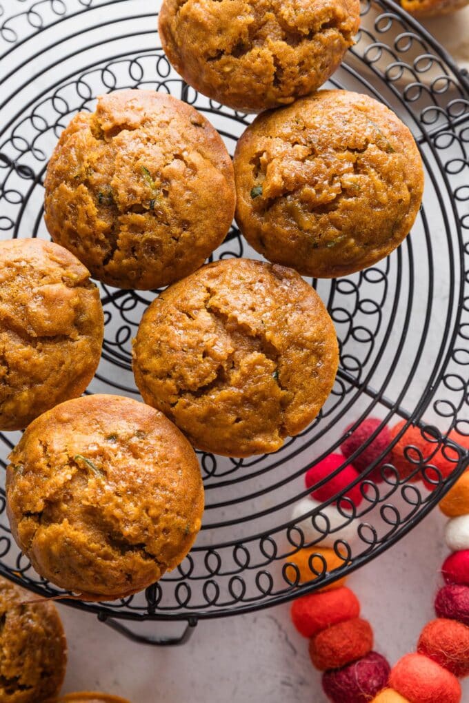 Large pumpkin zucchini muffins cooling on a black wire rack.