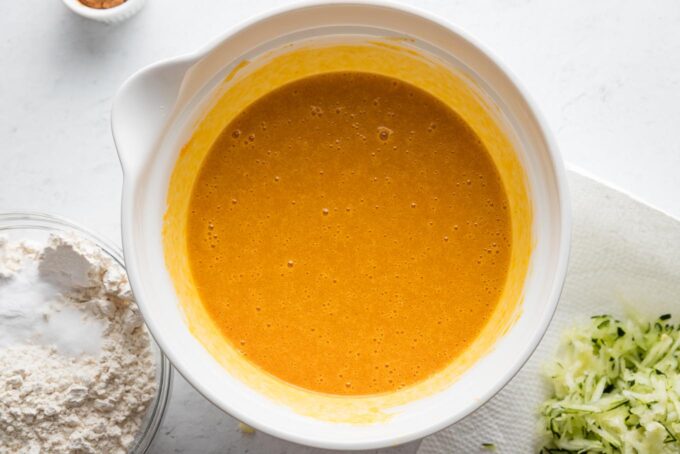 Wet ingredients for pumpkin muffins stirred together in a large white ceramic bowl.