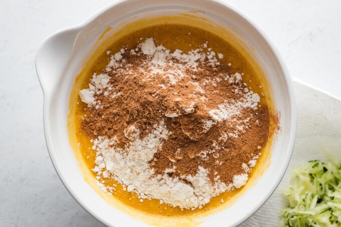 Flour, baking soda, and spices sprinkled on top of muffin batter in a bowl.