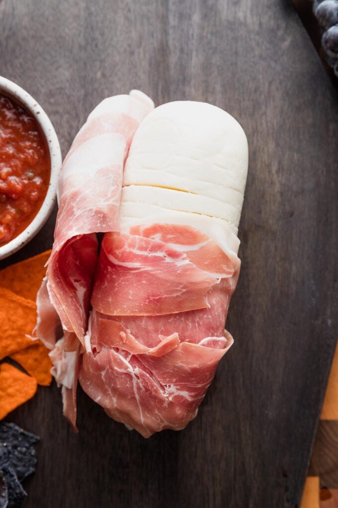 Opened mozzarella log partially wrapped in prosciutto.