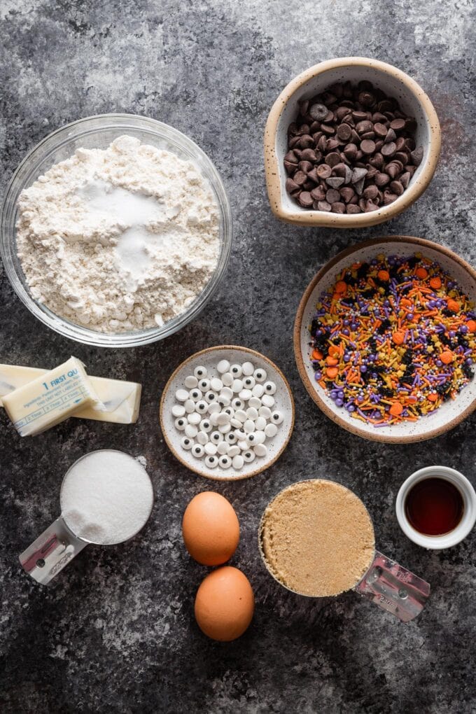 Overhead photo of flour, baking soda, salt, sugar, eggs, butter, vanilla extract, chocolate chips, and sprinkles, all ready to mix into a chocolate chip cookie dough.