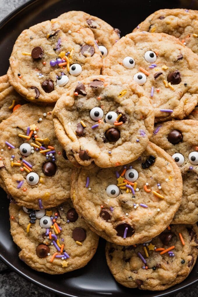 Close up of Halloween-themed chocolate chip cookies piled on a large black plate.
