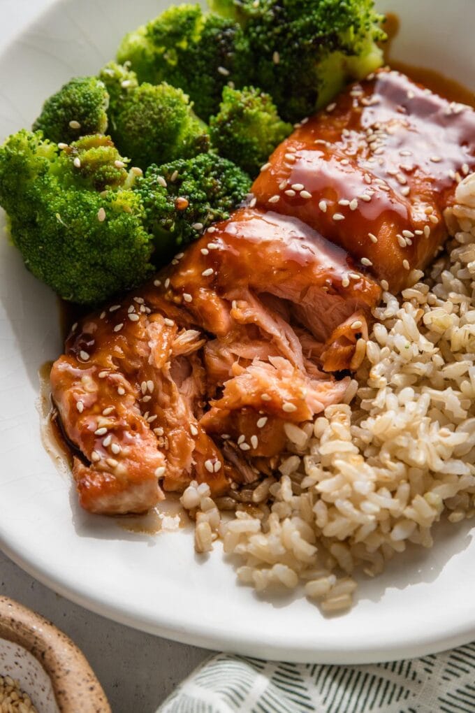 Close up of a flaky salmon fillet coated with teriyaki sauce and partially flaked apart with a fork.