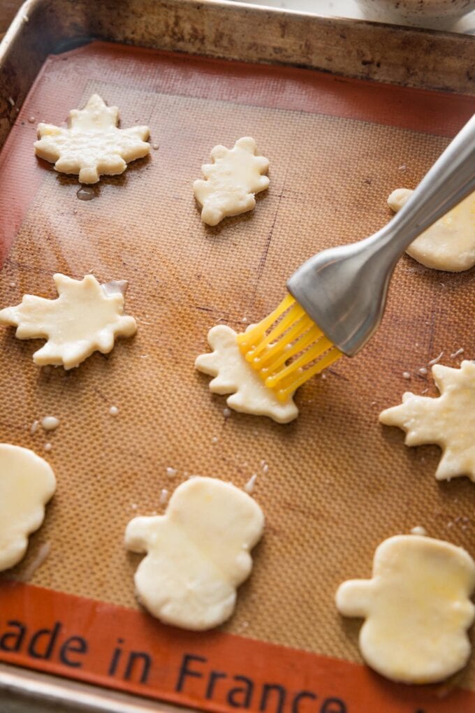 Pie crust leaves on a silicone baking mat being brushed with a light egg wash.