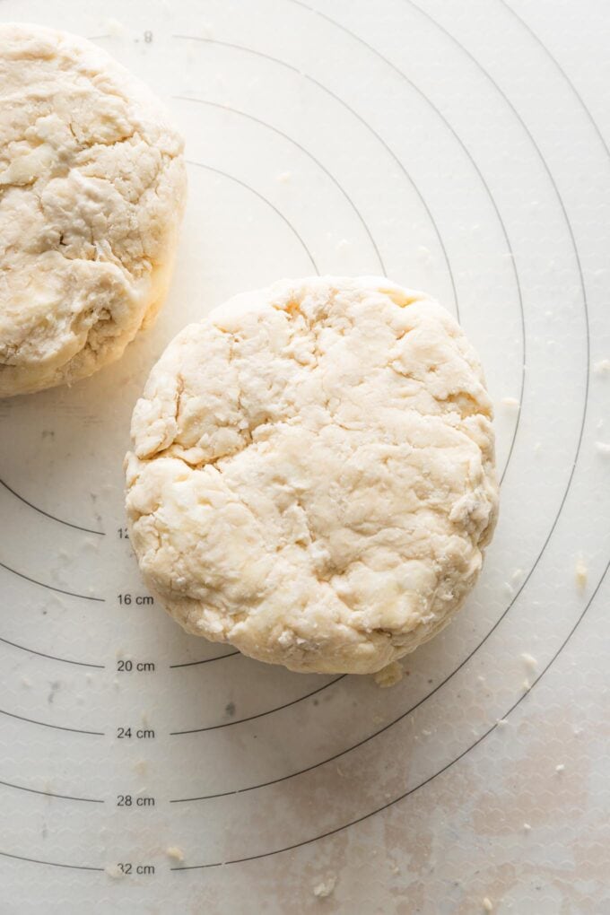 Two discs of pie crust dough just pressed and resting on a silicone pastry mat, with visible chunks of butter in the dough.