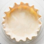 Close up overhead view of an unbaked pie crust made with all butter and apple cider vinegar, rolled out, pressed into a pie plate, and fluted around the edges.