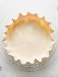 Close up overhead view of an unbaked pie crust made with all butter and apple cider vinegar, rolled out, pressed into a pie plate, and fluted around the edges.