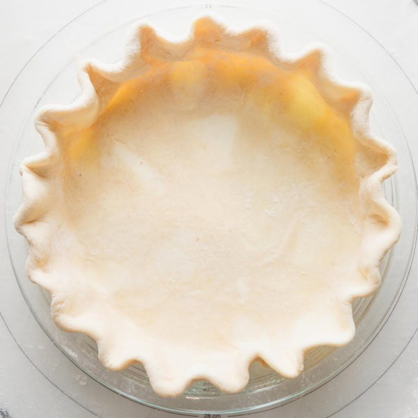 Close up overhead view of an unbaked pie crust made with all butter and apple cider vinegar, rolled out, pressed into a pie plate, and fluted around the edges.