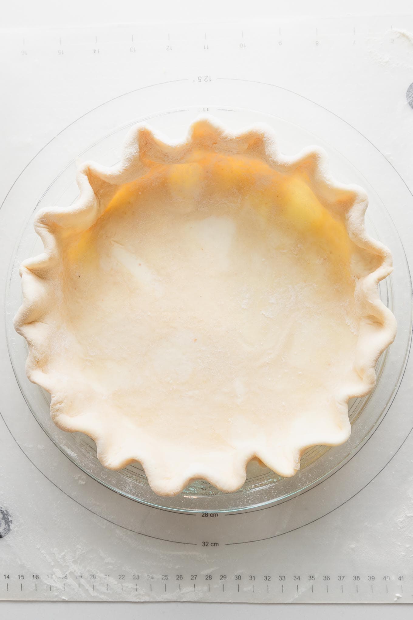 Close up overhead view of an unbaked pie crust made with all butter and apple cider vinegar, rolled out, pressed into a pie plate, and fluted around the edges.