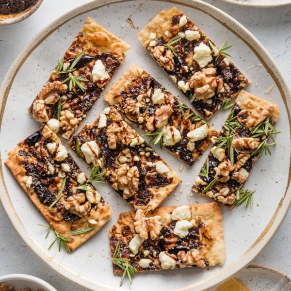 Flatbreads made with fig butter, toasted walnuts, feta, fresh rosemary, sliced and plated on a platter as appetizer bites.
