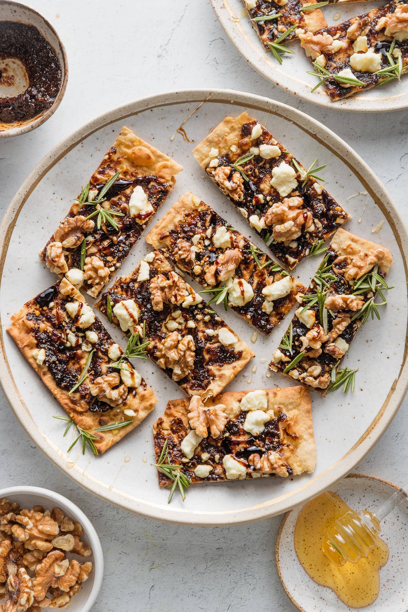 Flatbreads made with fig butter, toasted walnuts, feta, fresh rosemary, sliced and plated on a platter as appetizer bites.