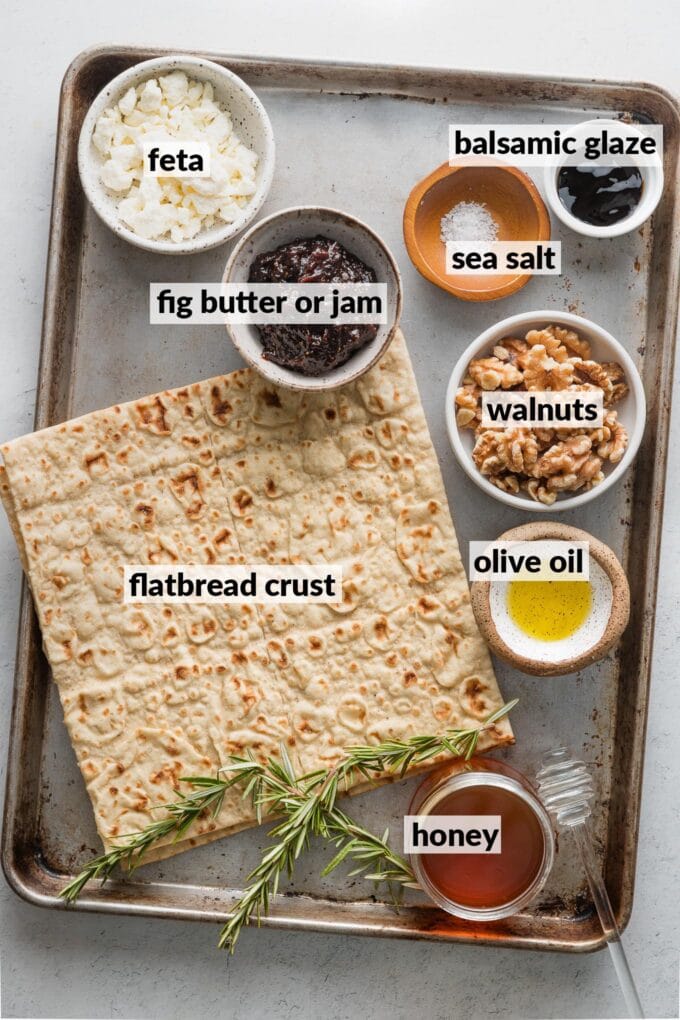 Labeled overhead photo of lavash style flatbreads, fig butter, feta, rosemary, walnuts, honey, balsamic glaze, and sea salt, all gathered and ready to make into an appetizer.