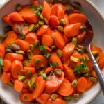Small serving bowl full of glazed carrots with fresh parsley, lemon juice, and pistachios.