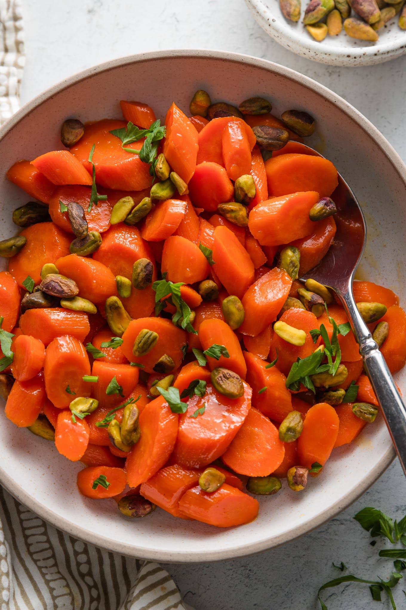 Small serving bowl full of glazed carrots with fresh parsley, lemon juice, and pistachios.