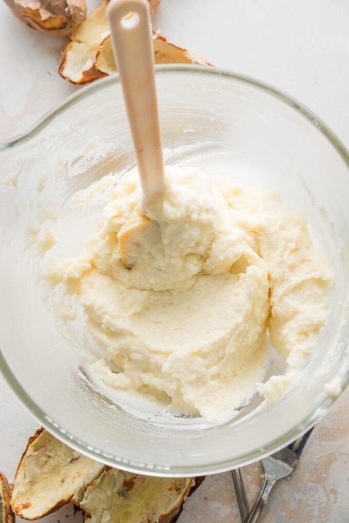 Spatula in the process of folding cream and butter into a large bowl of mashed potatoes.
