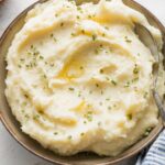 Bowl of creamy mashed potatoes with butter and chives.