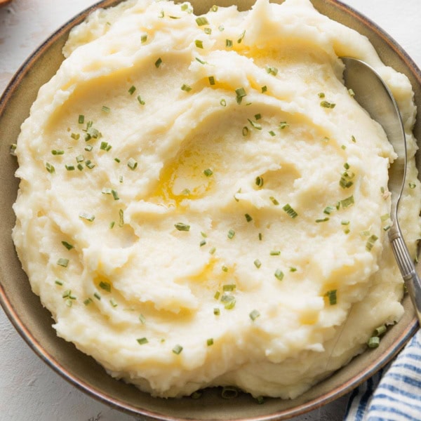 Bowl of creamy mashed potatoes with butter and chives.
