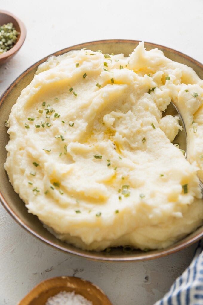 Bowl of make ahead mashed potatoes with extra melted butter and chives.