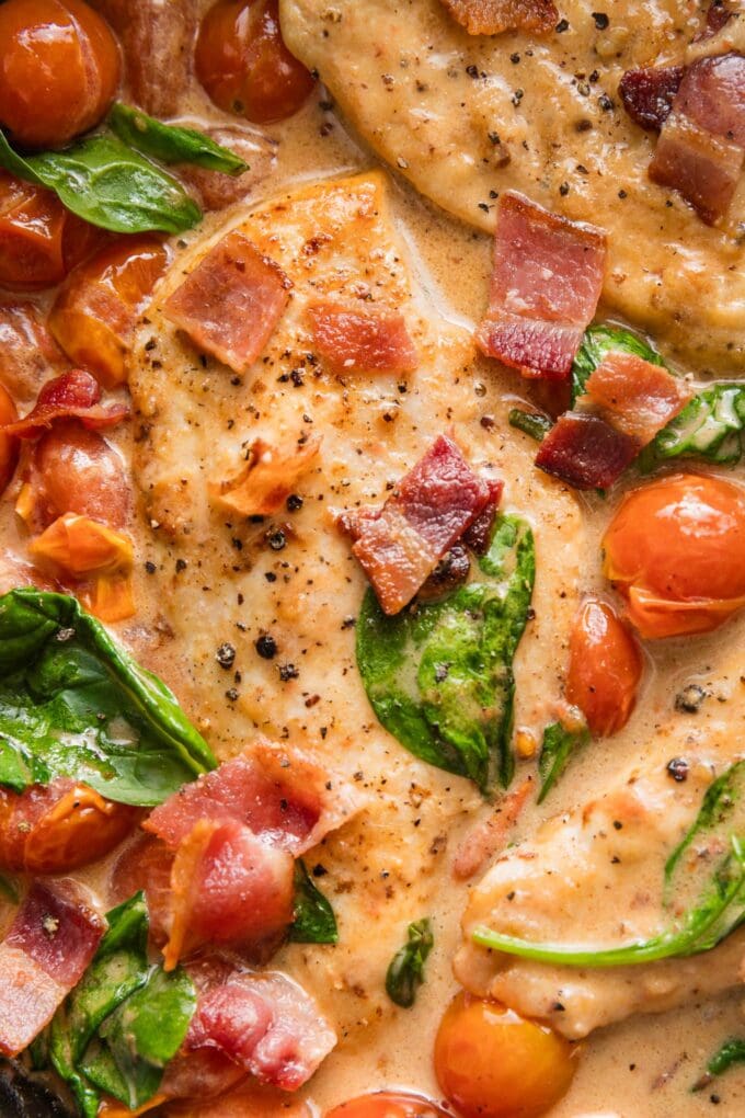 Close up image of chicken breasts seasoned and pan seared with cherry tomatoes, bacon, and baby spinach in a balsamic cream sauce.