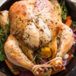 Cast iron skillet with a whole roast lemon butter chicken with carrots, potatoes, and herbs.