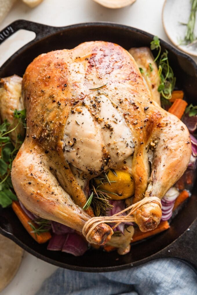 Cast iron skillet with a whole roast lemon butter chicken with carrots, potatoes, and herbs.