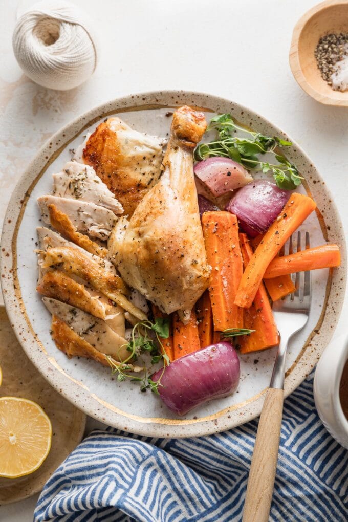 Plate filled with pieces of a whole roast lemon chicken, carved and served with roasted carrots, onion, and herbs.