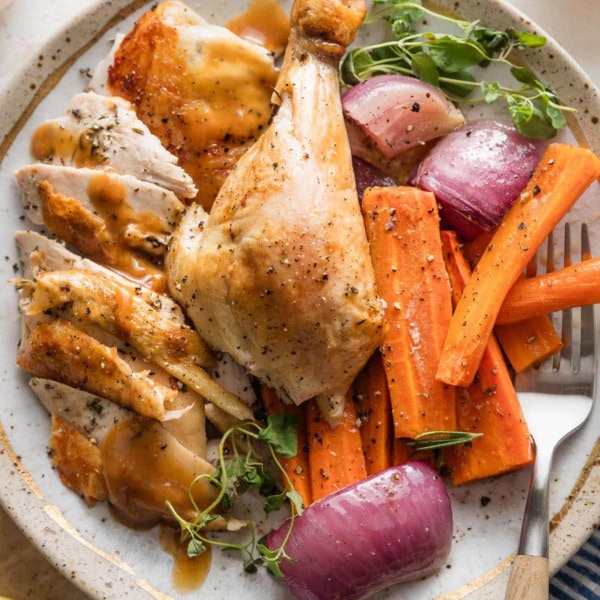 Plate with pieces of a whole roast lemon chicken served with roasted carrots, veggies, and herbs.