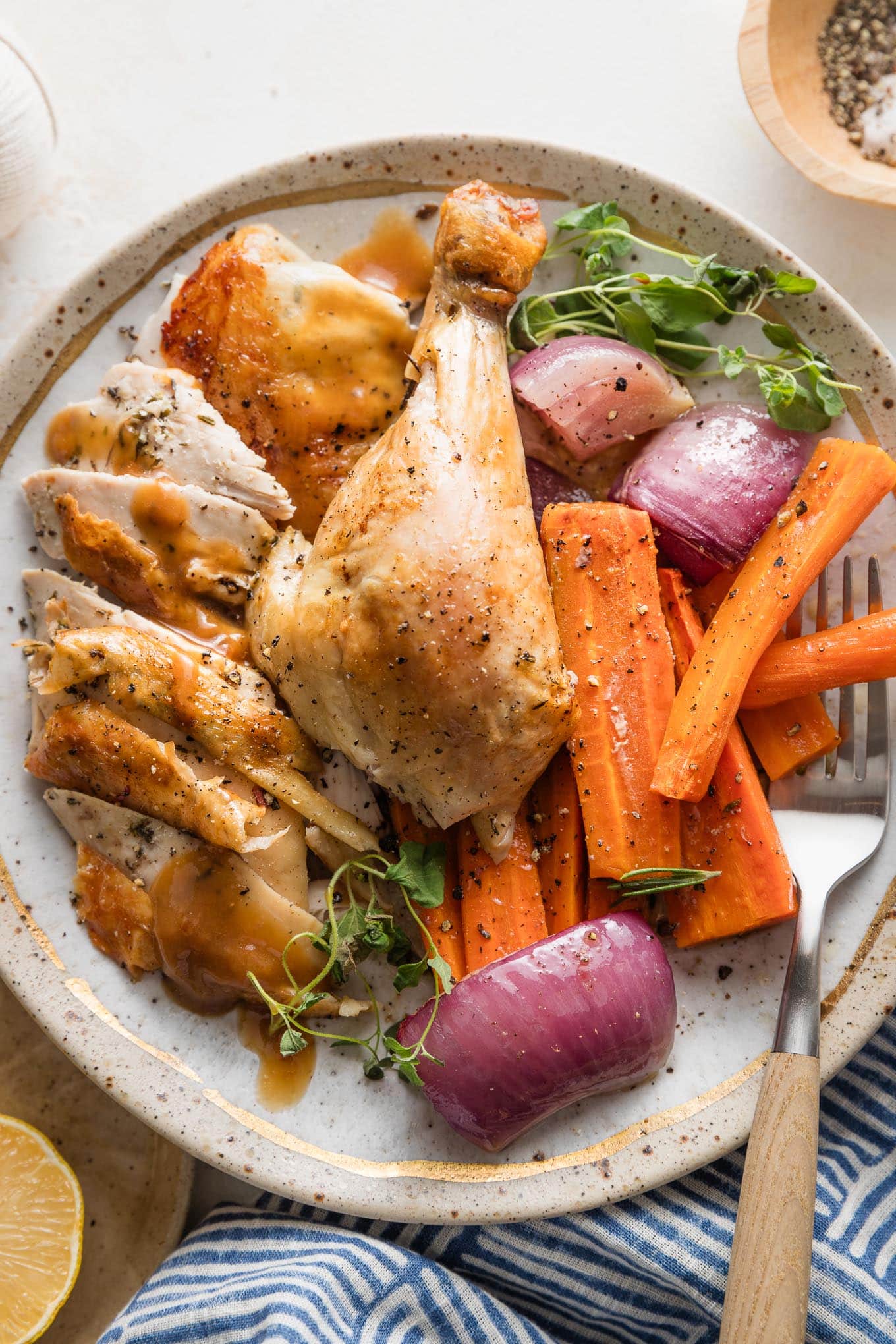 Plate with pieces of a whole roast lemon chicken served with roasted carrots, veggies, and herbs.