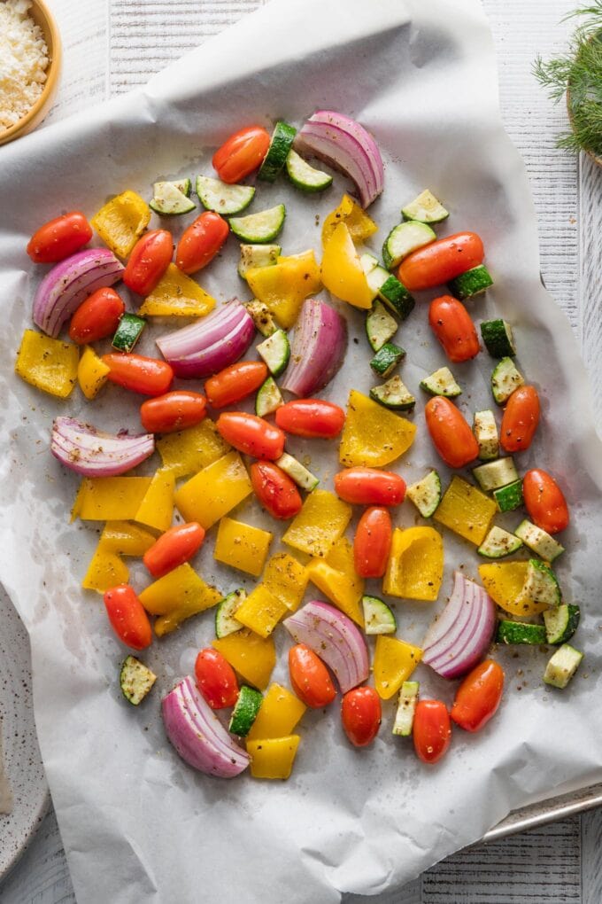Zucchini, onion, pepper, and tomatoes spread out to roast on a large baking sheet.