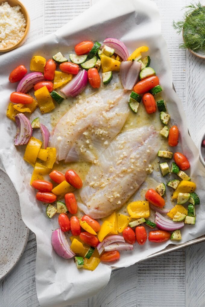 Tilapia added to a roasting pan with Greek-inspired veggies and lemon butter sauce.