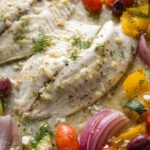 Close up of Greek tilapia on a sheet pan with veggies and olives.