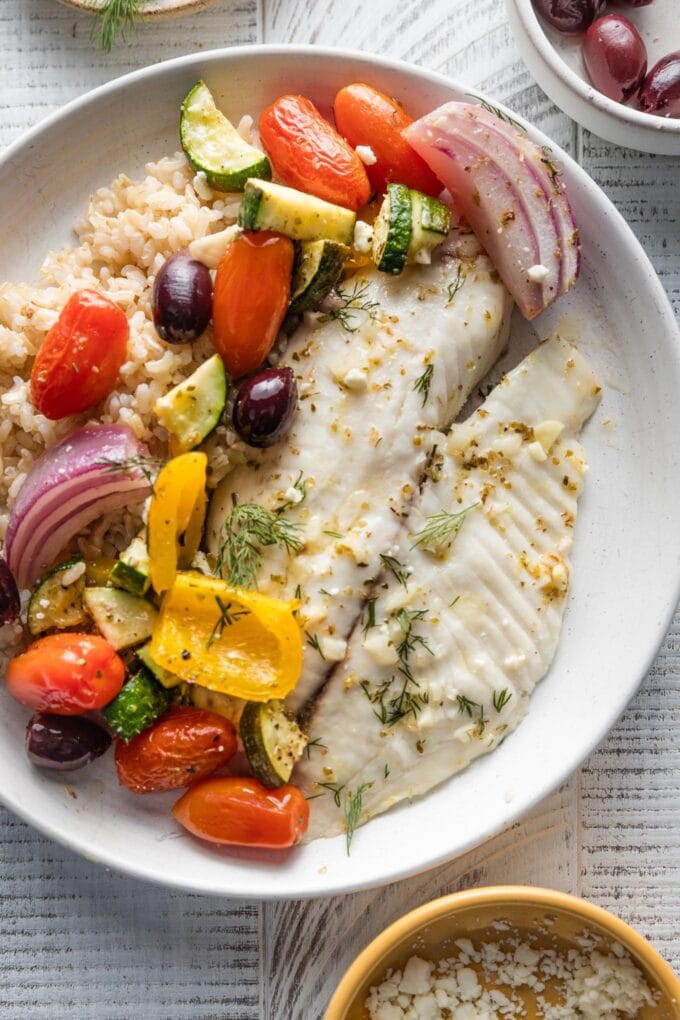 Plate with a helping of Greek-seasoned tilapia, roasted veggies and Kalamata olives, dill, and brown rice.