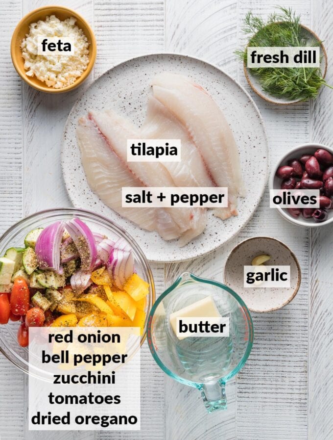Labeled overhead photo of tilapia seasoned with salt and pepper; chopped zucchini, pepper, and tomatoes seasoned with olive oil and oregano; feta, dill; olives, butter, and garlic.